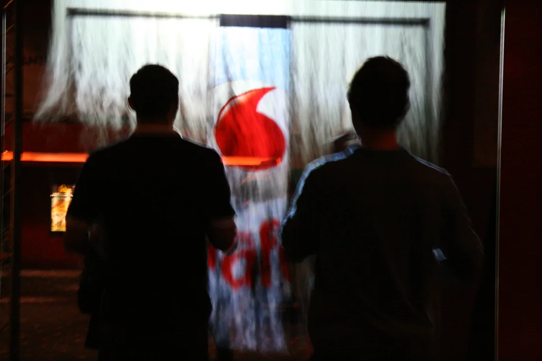 Návštěvníci před mlžnou projekcí loga Vodafone.